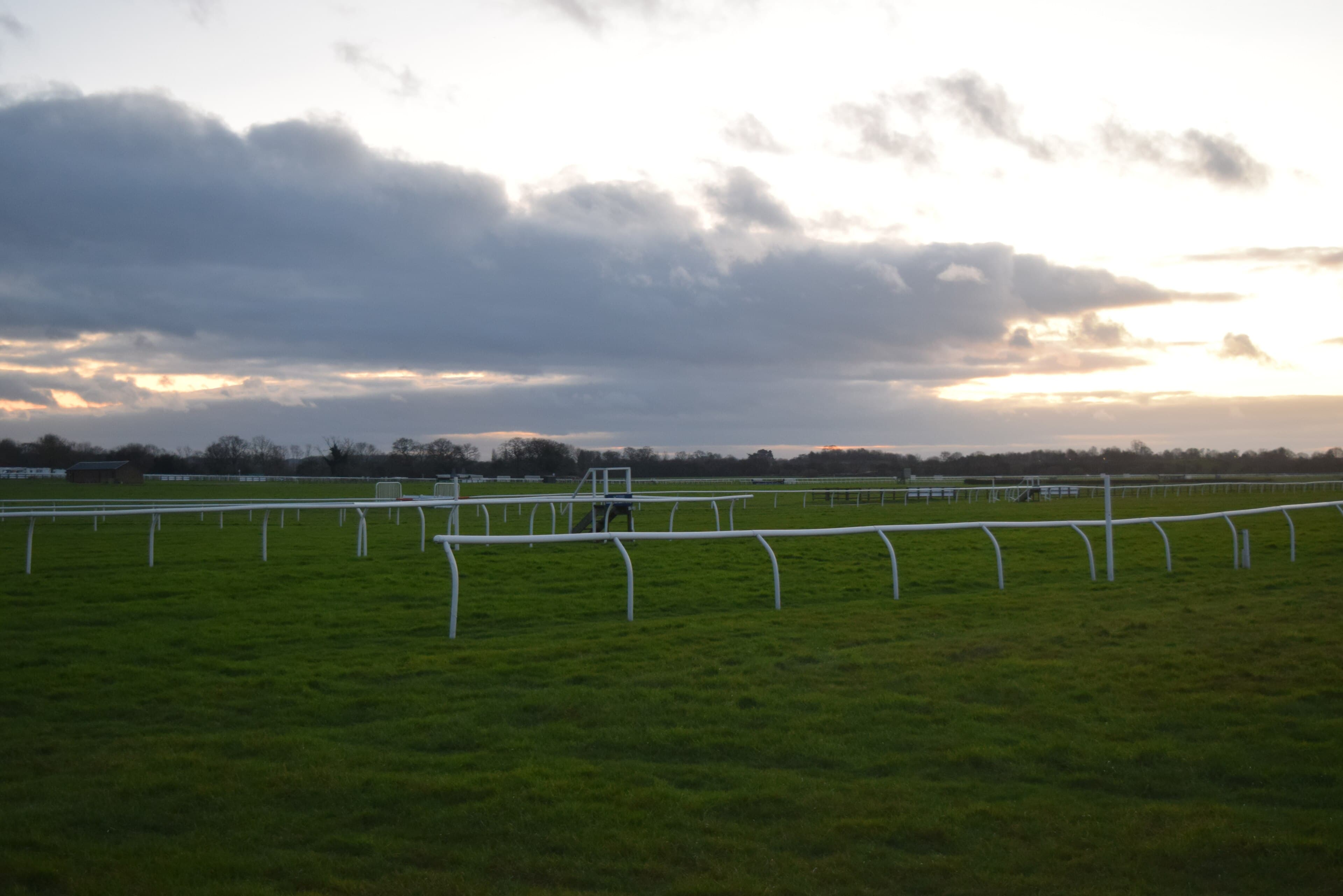 The rails and hurdles of Wetherby racecourse under a winter sunset, with the far-side buildings low on the horizon.