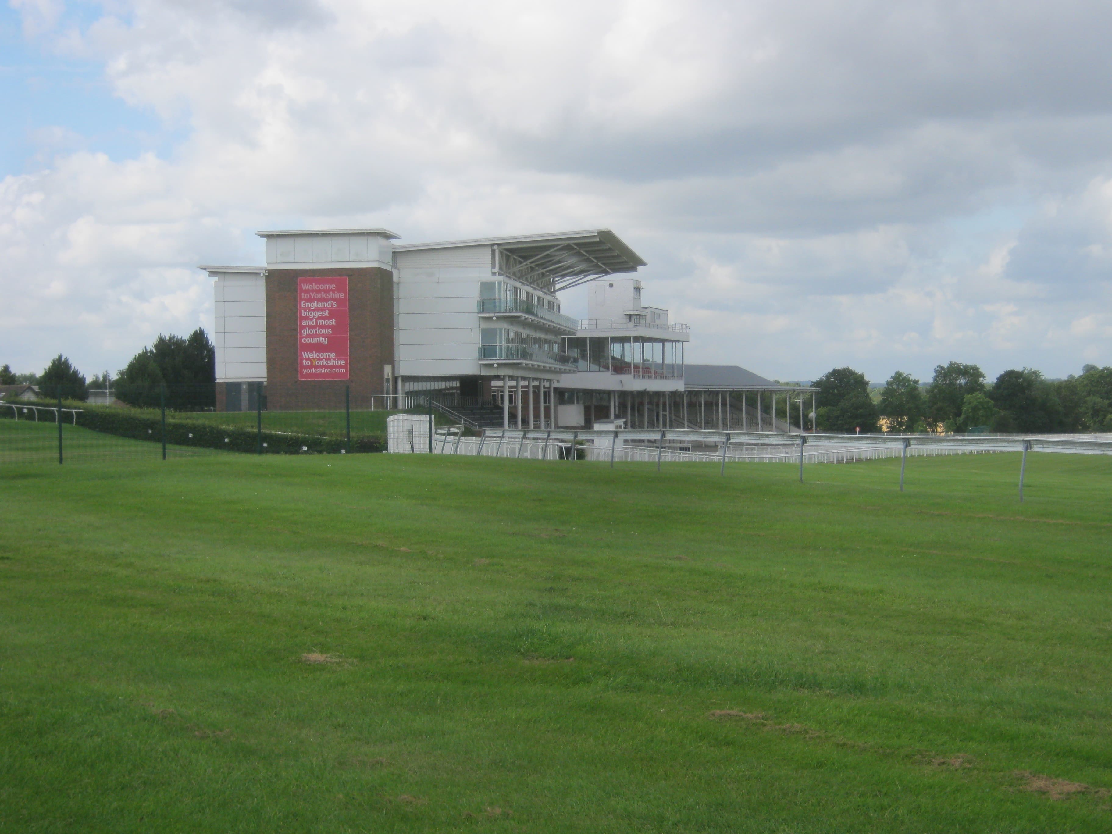 The main grandstand at Wetherby racecourse seen across the turf, a tall red-brick and glass building with a cantilevered roof.