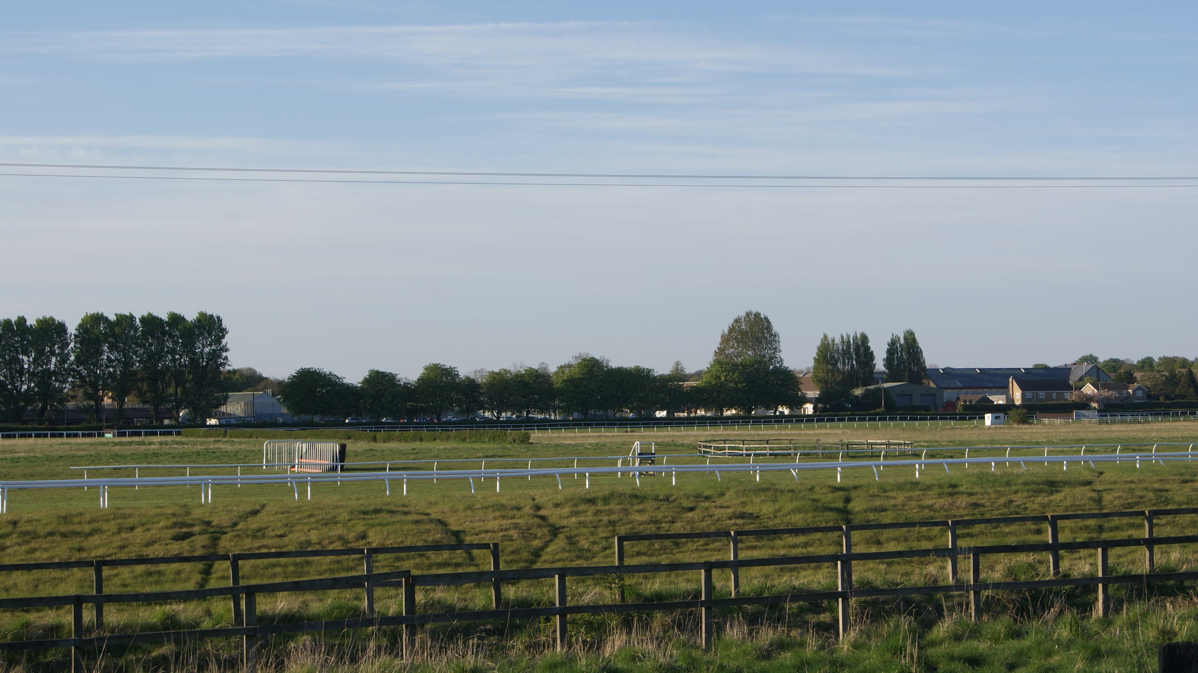 Wetherby racecourse seen from the Harland Way footpath, with the running rails and a set of hurdles across the grass.