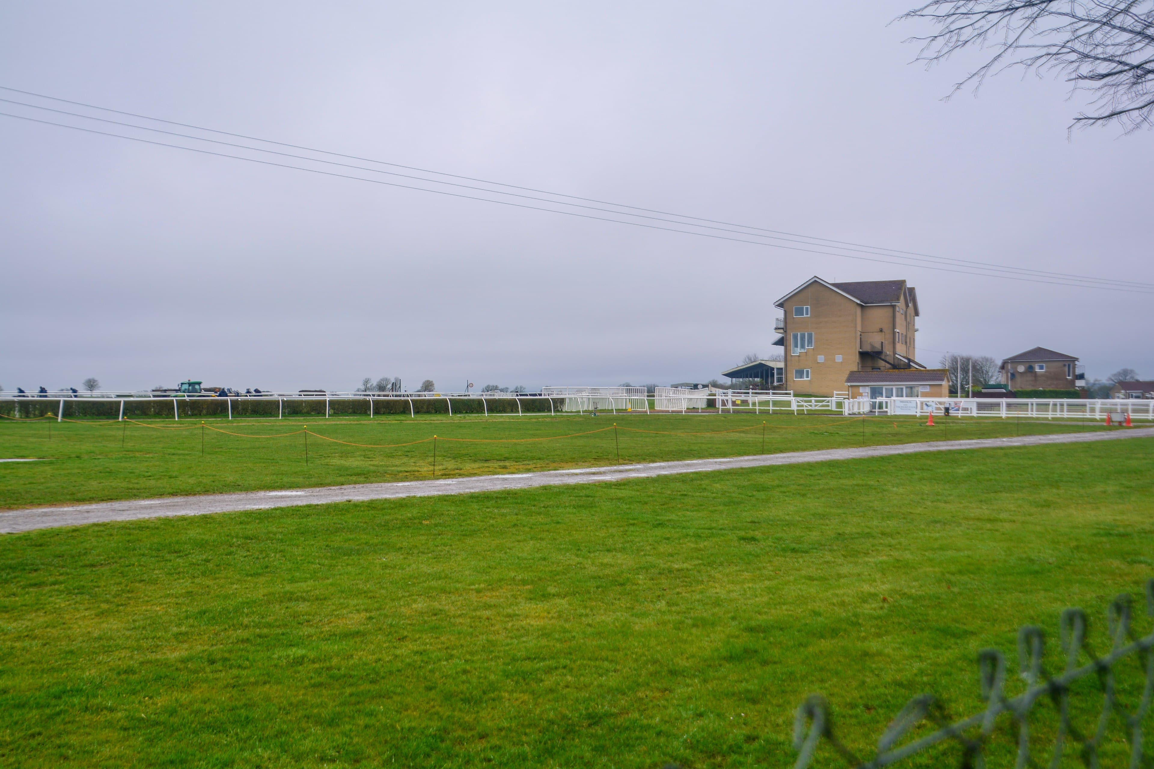 The track at Wincanton racecourse on a grey winter day, with the white running rails and the stone-built stand beyond.