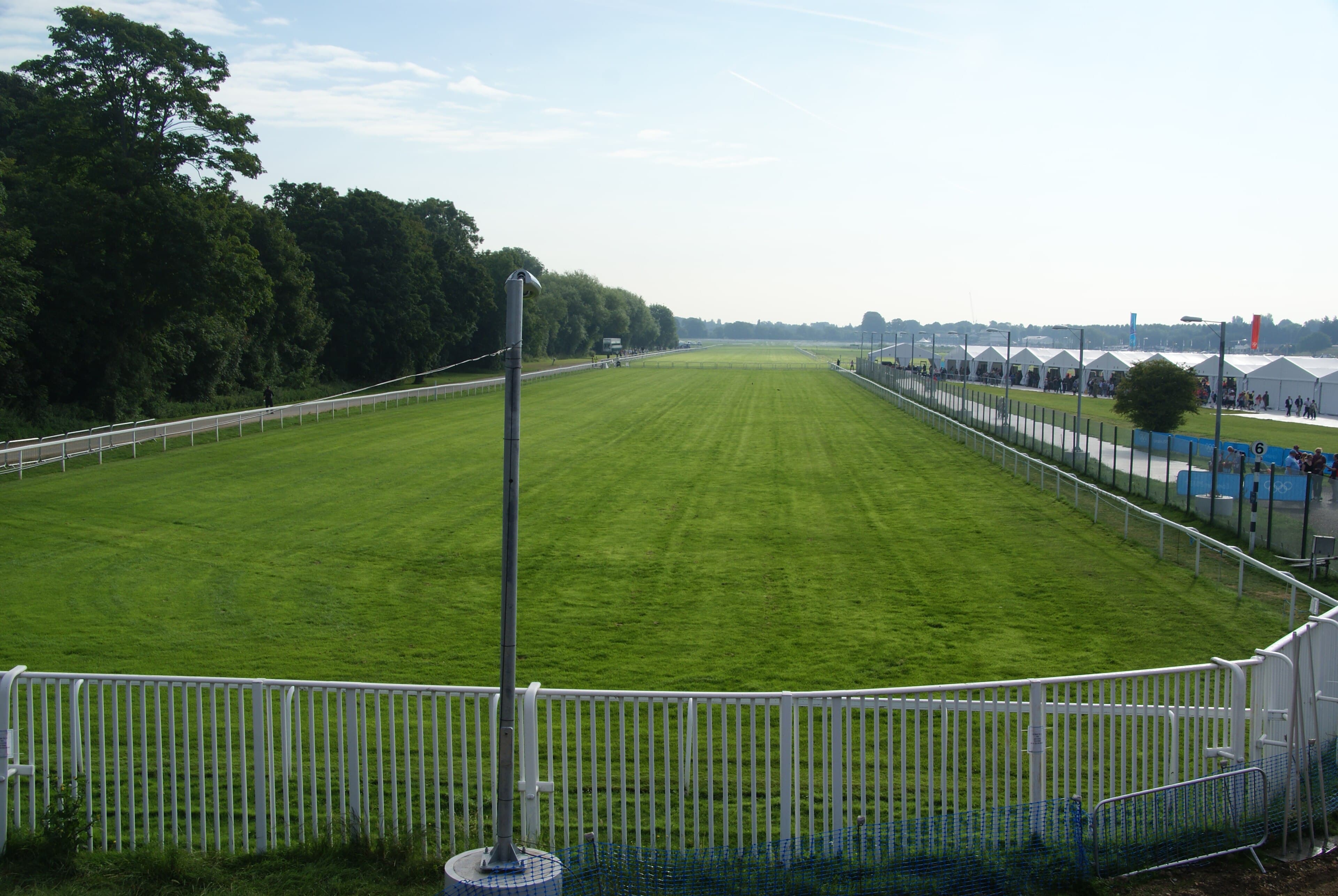 Looking down the straight mile at Royal Windsor racecourse, with rails on both sides and marquees along the far rail.