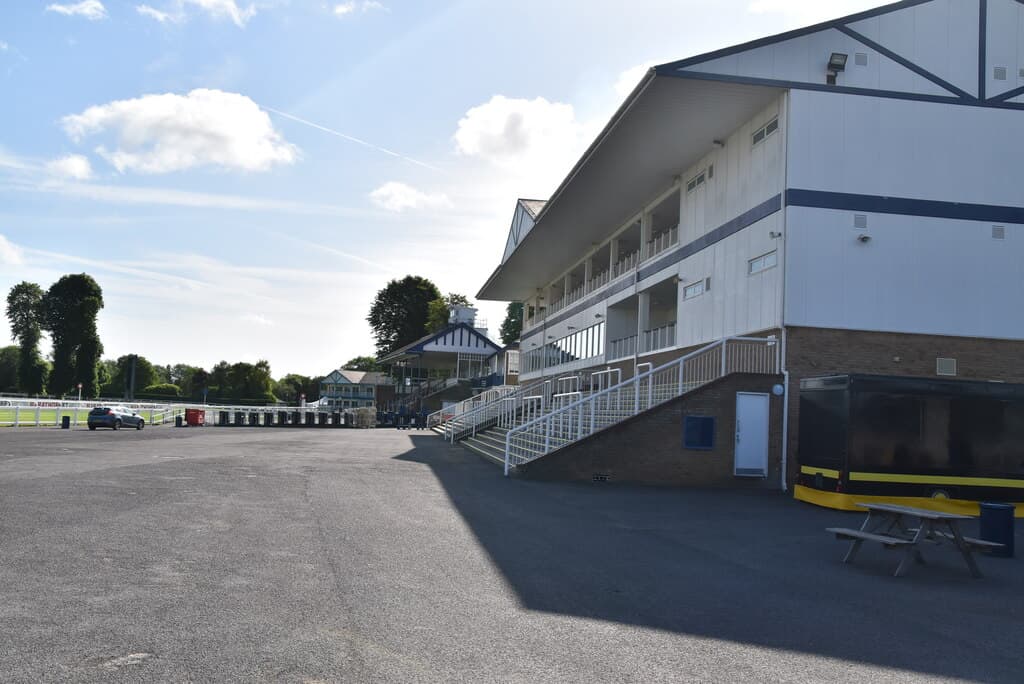 The stand building at Royal Windsor racecourse seen from the tarmac apron behind it on a bright day.