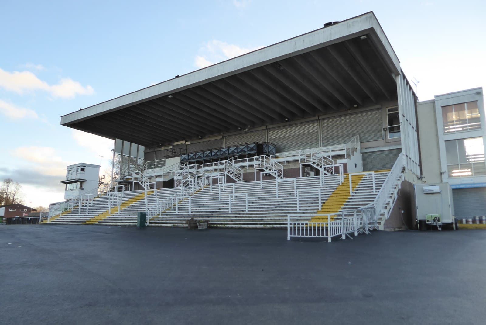 The open-fronted grandstand at Worcester racecourse from the tarmac apron, its cantilevered roof over tiered seating.