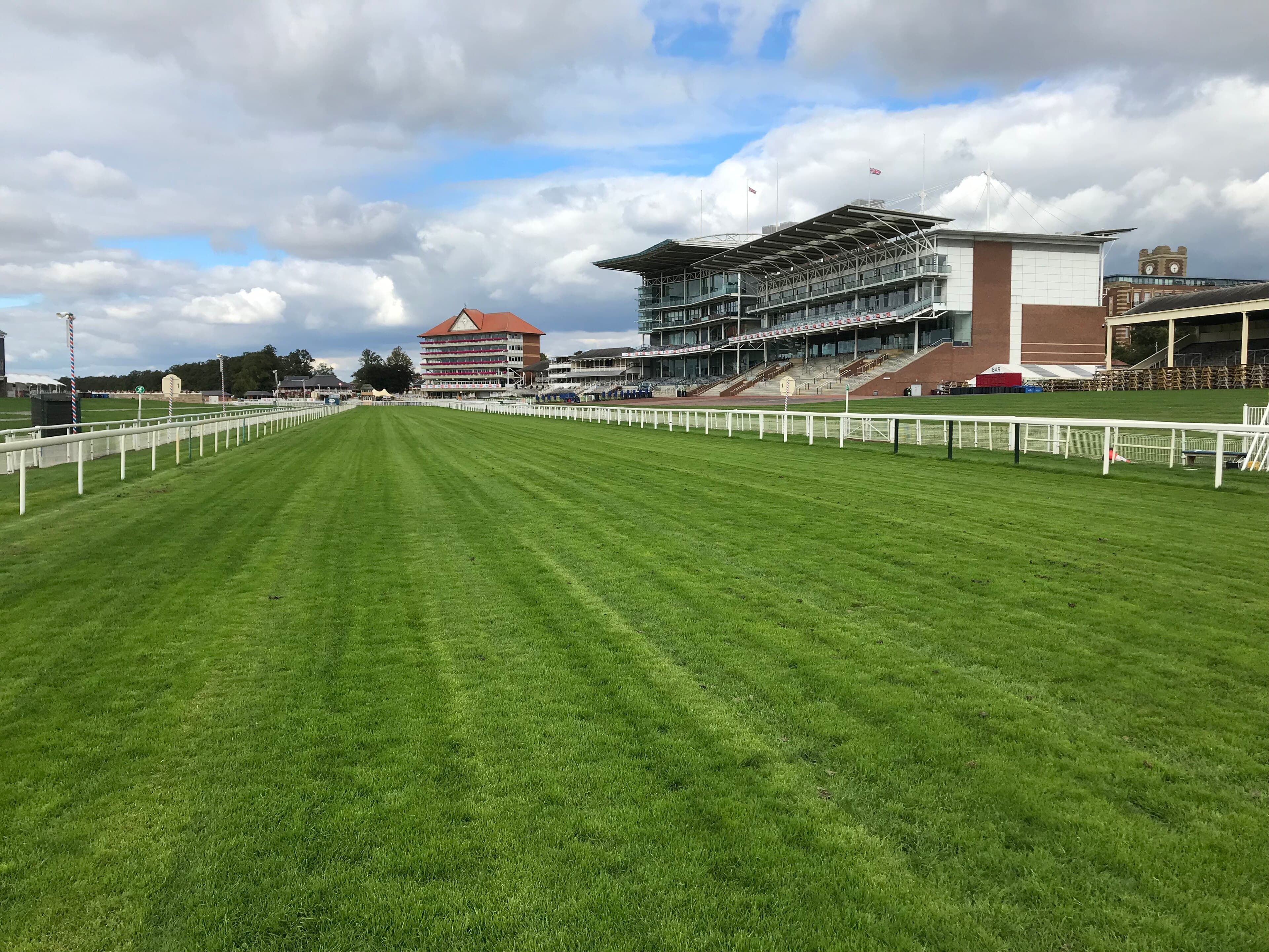 The finishing straight at York with the Knavesmire and Ebor stands along the rail and broken cloud above.